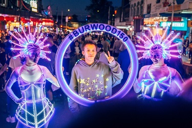 two women in illuminated outfits holding illuminated circle with #burwood150,  with boy posing in centre of circle