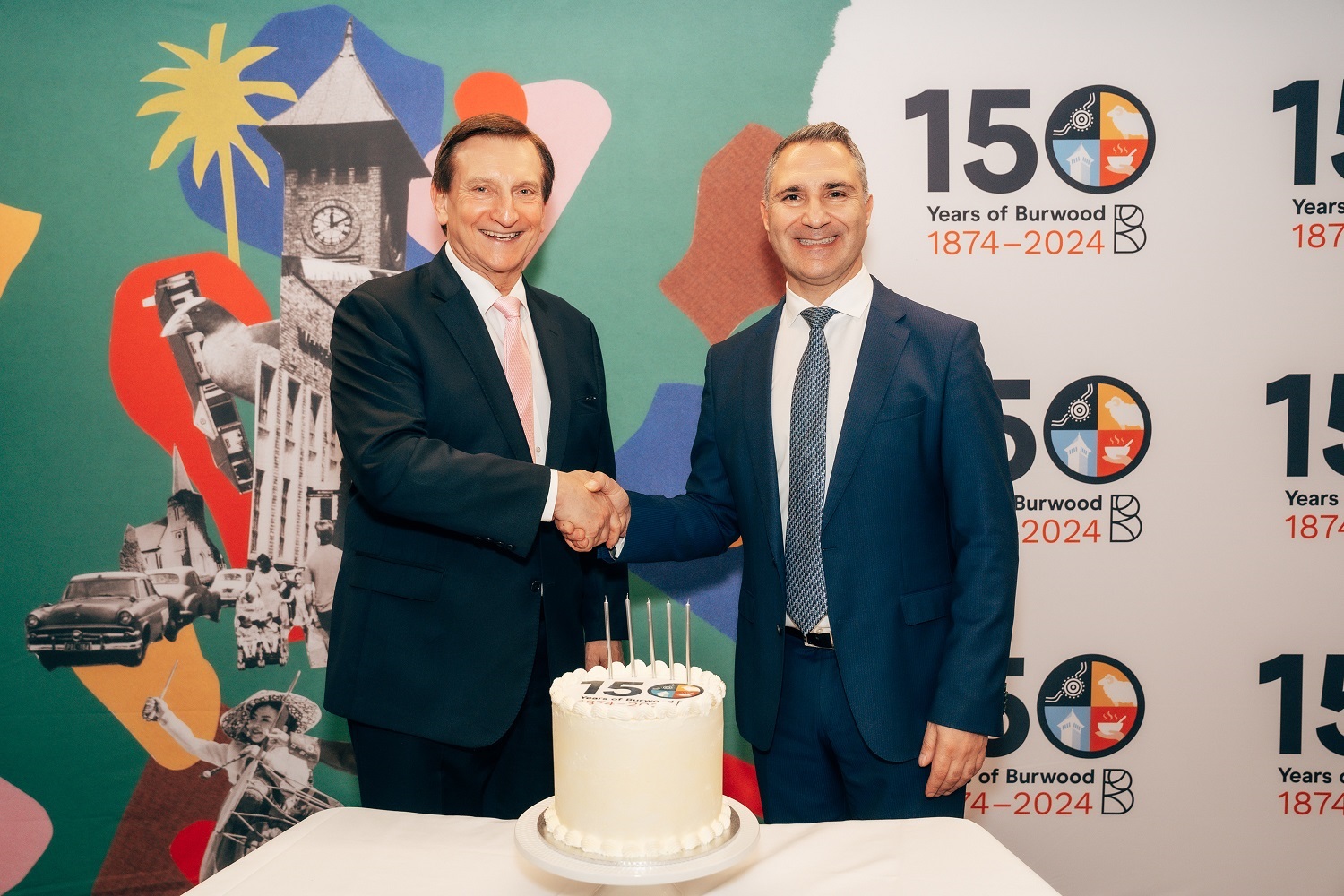 Mayor John Faker and the Minister for Local Government Ron Hoenig shaking hands with 150 Year birthday cake on a table